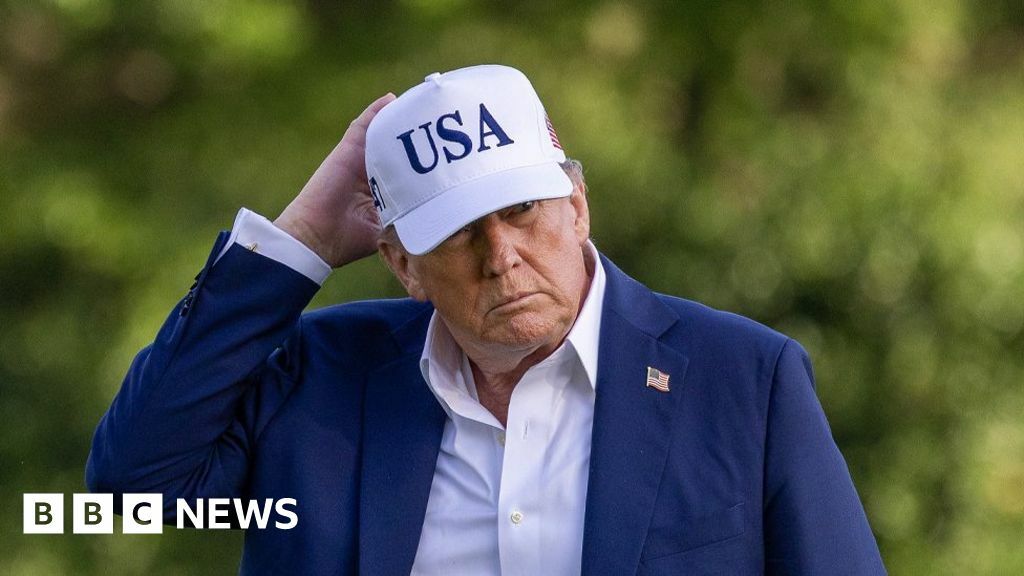 US President Donald Trump wearing a blue suit and a white cap with USA on it