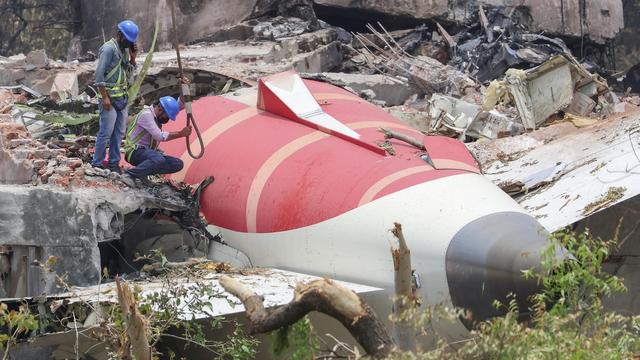 Des gens avec des casques bleus essaient de dégager une carcasse d'avion de décombres.