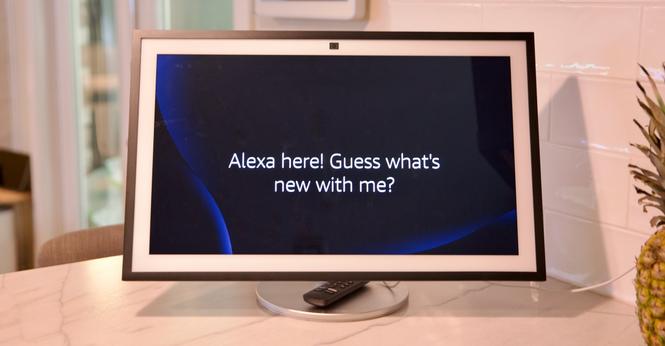 A large smart display on a kitchen counter displaying the words “Alexa here! Guess what’s new with me?”