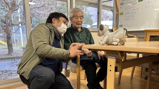 Les deux hommes regardent un petit chien robotisé.