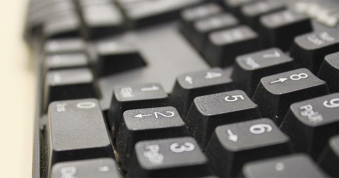 Teclado de computador em close, com as teclas direcionais e de números, na cor preta, em primeiro plano