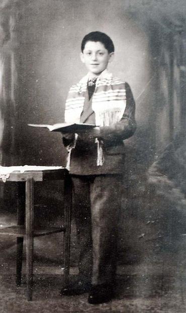 Young boy standing beside a small table, holding an open book.