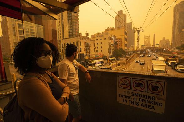 People wear masks as they wait for the tramway to Roosevelt Island as smoke from Canadian wildfires casts a haze over the area on June 7, 2023, in New York City.
