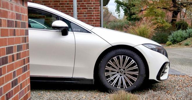 Mercedes EQS lugt hinter Hauswand hervor.