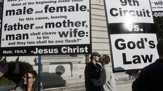 Aiden Lougee, center left, kisses his boyfriend, Rex Resa, seen between signs held by opponents to gay marriage outside of the courthouse after a hearing in the Ninth Circuit Court of Appeals, Monday, Dec. 6, 2010, in San Francisco. (AP Photo/Jeff Chiu, File)
