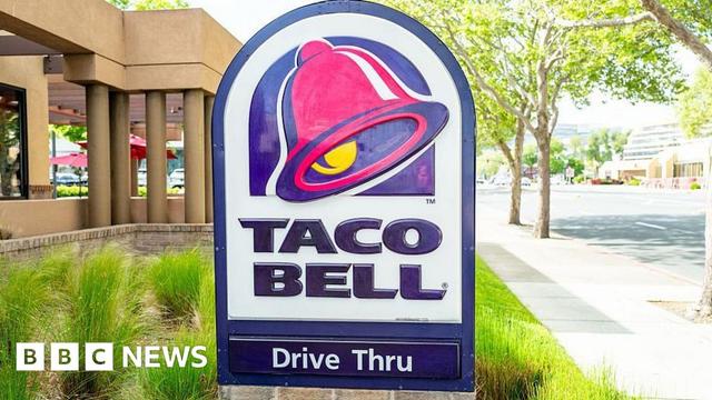 A Taco Bell Drive Thru sign showing the pink and yellow bell and purple text saying 'Taco Bell, Drive Thru'.