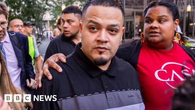 Kilmar Ábrego García wears a black and grey top surrounding by several people as he walks through a crowd.