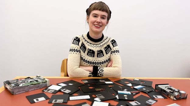 A smiling woman with her arms folded sits in front of a table with floppy disks scattered across it (Credit: Cambridge University Library) A smiling woman with her arms folded sits in front of a table with floppy disks scattered across it (Credit: Cambridge University Library)