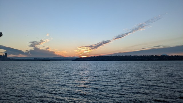 The sun rises behind the mountains, reflecting off the waters of Puget Sound.