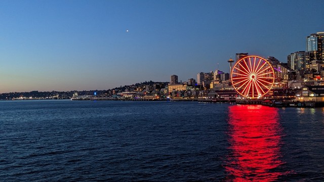 The Seattle Great Wheel, glowing red, reflects on the waters of Puget Sound at dusk.
