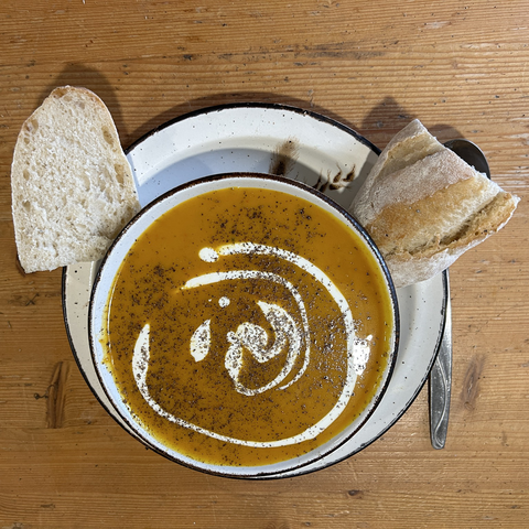 A bowl of pumpkin soup (with a swirl of sour cream on top) and two pieces of home-baked bread.