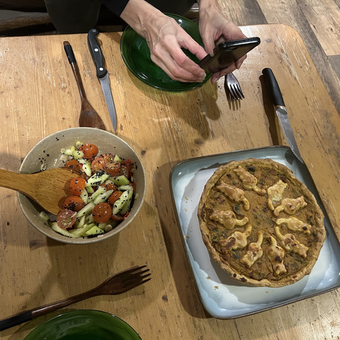 Dinner for two: a pie, decorated with cat-shaped bits of dough on top, plus a tomato & cucumber salad. Also in the frame: parts of the hands and phone of my houseguest who's taking a pic of the pie. It is a cute pie, with the cirkle of ten dough cats on top, their tails pointing at the centre of the pie. 