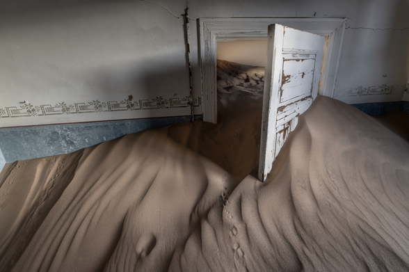 Inside of room in an abandoned building in the desert, sand is almost to the top of and open door.