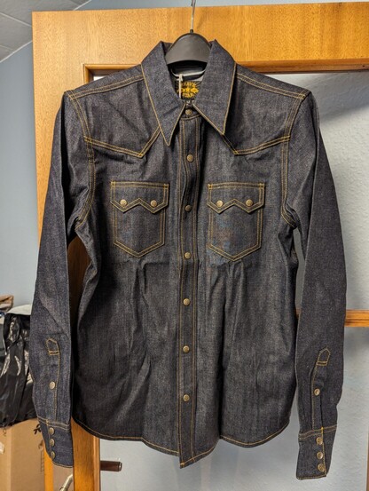 Front view of a western style denim shirt with sawtooth pockets and brass snap buttons.
