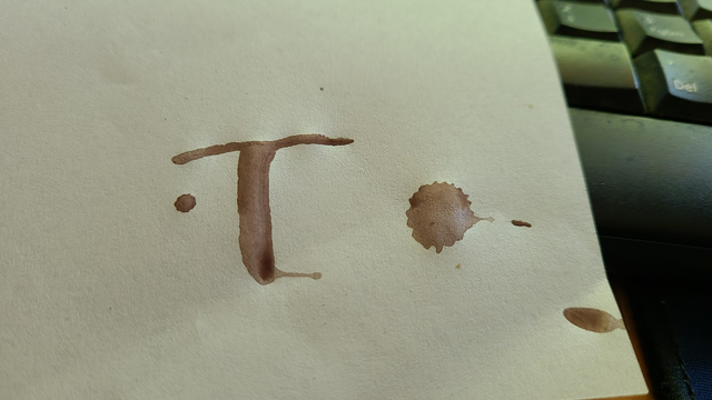 A piece of white paper with some drops and the letter T in brown ink.