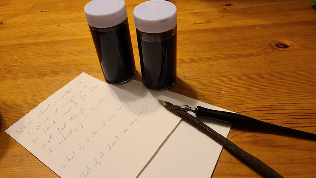 Two glass spice jars of dark ink, a metal nibbed dip-pen, and a sharpened stick sitting beside a writing sample that reads:
What about a metal nib? 
I think it might not be thick enough for this
not bad though
I actually quite like this.

What if I do use some honey?
What if I don't use any honey?