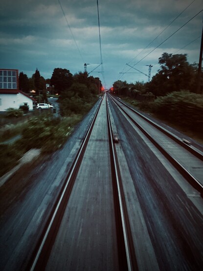 Schienen aus dem Fenster des letzten Zugwagons fotografiert. Abendstimmung. Rote Lichter.

Rails photographed from the window of the last train wagon. Evening mood. Red lights.