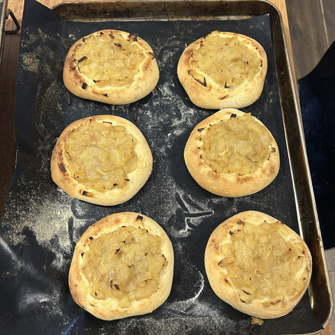 Closeup from above of six finished onion breads still on the oven tray. The crust is nicely coloured