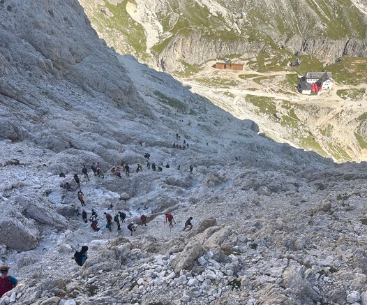 Lots of hikers on the trail down from Rifugio Alberto 1 to Rifugio Vajolet, visible down in the distance. A traffic jam composed of hikers.