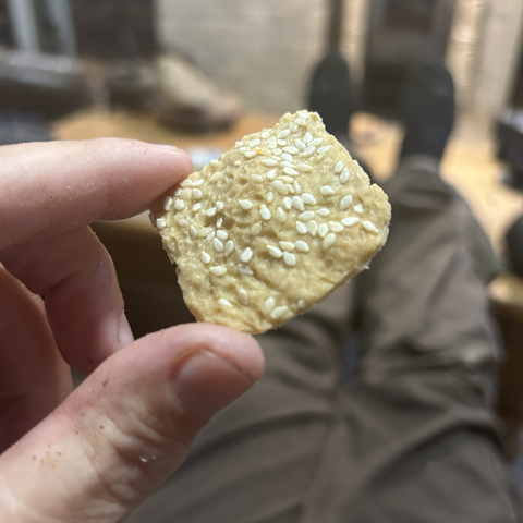 Extreme closeup of one cracker that I hold between thumb and index finger. It's only ever so slightly browned (more yellow than brown) but that's what you want with these. The white of the sesame topping still stands out against the cracker proper. It really looks appetising - and the poor thing didn't survive the photo shoot by more than a second or two. 