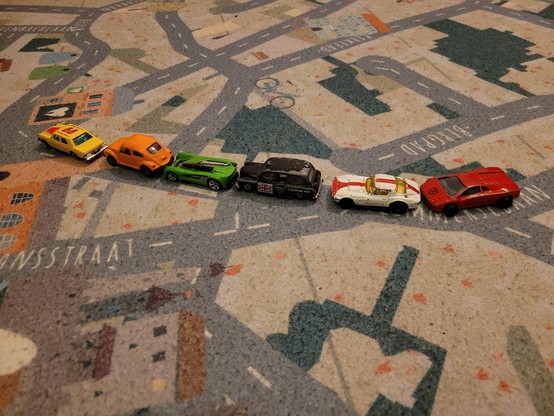 A row of toy cars on a playmat with a map on it.