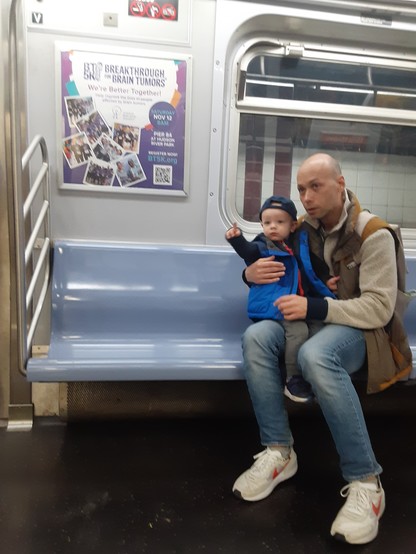 Father holding small son on his lap-- son pointing and excited about his first train ride on the NYC subway. Photo by Shell Sheddy 
