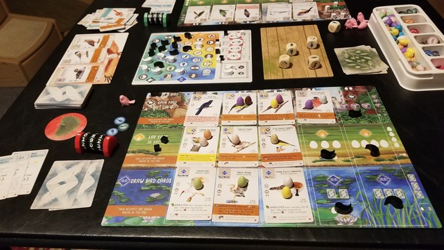 A completed game of Wingspan Asia is set out on a card table. There is an organized clutter of bird cards, bonus cards, food dice, round food tokens, and plastic egg tokens.