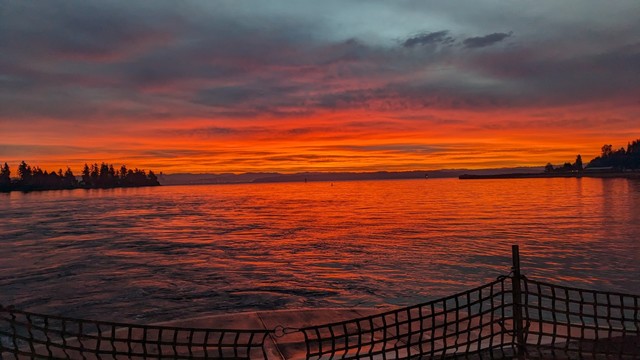 The sun rises, scarlet red, reflecting off the waters of Eagle Harbor. The safety net of a ferry can be seen in the foreground.