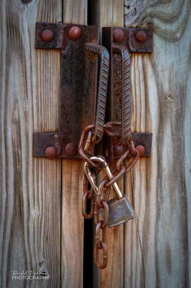 Rusty homemade door handles made of steel plate and rebar are chained together and locked. 