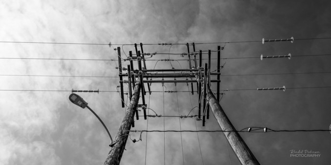 Looking up at 2 power poles with multiple electrical wires. 