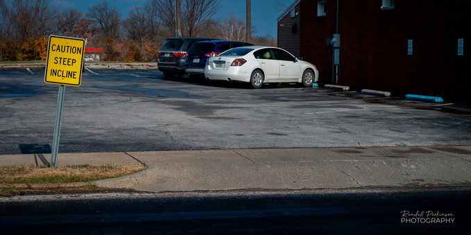 Flat parking lot with a sign at the entrance saying, "CAUTION STEEP SLOPE".
Weird. 