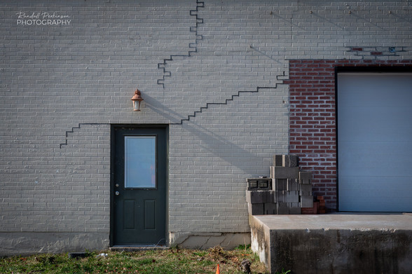 The back side of a commercial building where cracks in a light colored brick wall that have been filled with black caulking. 