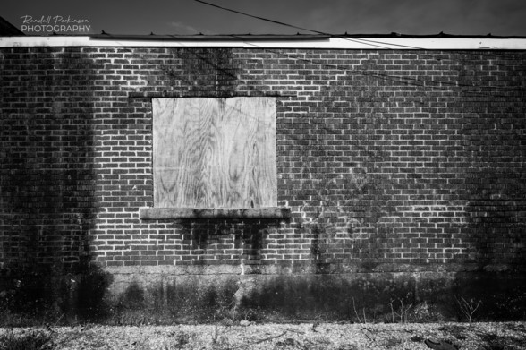 Brick wall with apparent burn marks and a boarded up window. 