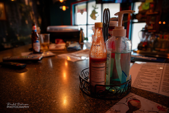 Bar top with hot sauce and hand sanitizer bottles. 