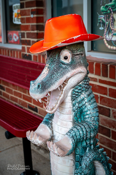 A statue of a Gator wearing an orange cowboy hat stands in front of a brick restaurant building. 