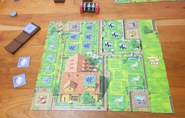 My Zooloretto board at game end. Zebra, elephant, panda, and flamingo tiles are grouped into their own enclosures.  An extra elephant is hanging out in the barn area.