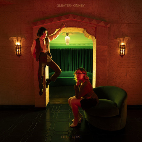 Sleater-Kinney sit or levitate in a dim room with an arched doorway on the cover of the album Little Rope from 2024. 