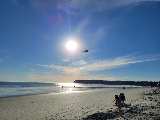 Beach view, with a military helicopter against the sun, kids playing in the distance.
