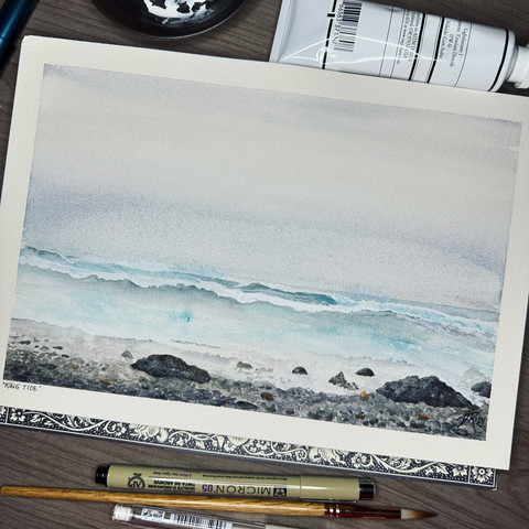 A watercolor painting of the ocean during a king tide, an extreme tidal event at the Oregon Coast. The waves foam up against black rounded cobbles on the beach, with large white waves cresting and crashing further from shore, with large sprays shooting up against the horizon. The water is faintly blue-green and the skies are muted grays.