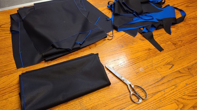 Three piles of cut fabric and a pair of scissors on a wooden floor.