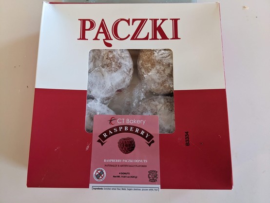 A red-and-white box, with white on top and red below like the Polish flag, labeled Pączki. A clear plastic window shows four pączki inside; the label reads "Raspberry."