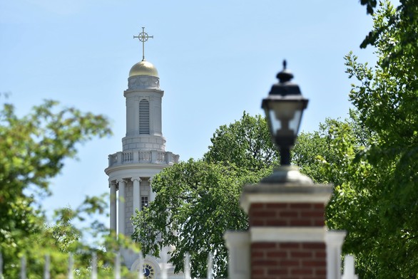 In the background, a tall white steeple with gold dome and sunburst cross. In the foreground, in soft focus, a brick post with a lantern on it in black iron.
