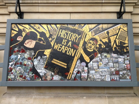 A mosaic of a protesting worker holding up a giant book with the legend "HISTORY IS A WEAPON / Nothing is Inevitable / Everything is Possible" in the middle of a protest scene, as helmeted police beat the crowd with batons. There are alos many small images of political protest around the world.