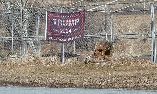Across from the entrance to the nature reserve, a TRUMP 2024 FUCK YOUR FEELINGS flag hanging on a fence.