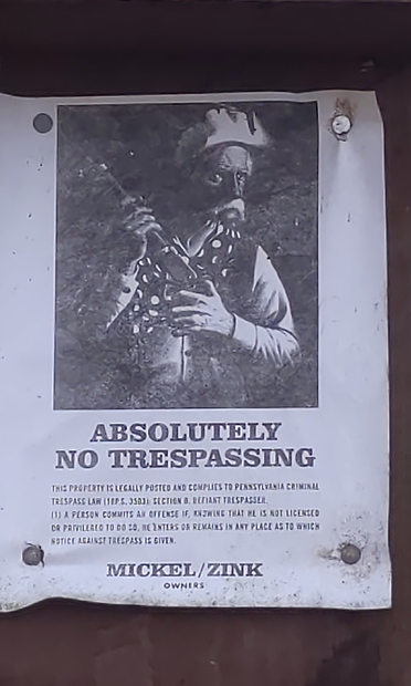 An unusual No Trespassing sign with a photo of a man in a white hat a white moustache holding a rifle that says:
ABSOLUTELY
NO TRESPASSING
some small print that begins with "This property is legally posted ...."
At the bottom.
MICKEL / ZINK
OWNERS