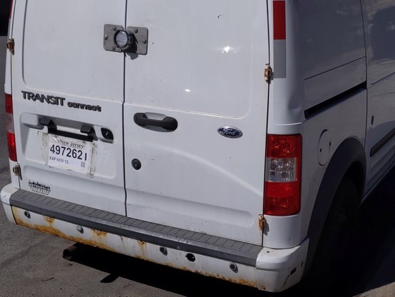 Rear of parked white Ford Transit with temporary NJ License Plate showing month and day expired but no year.