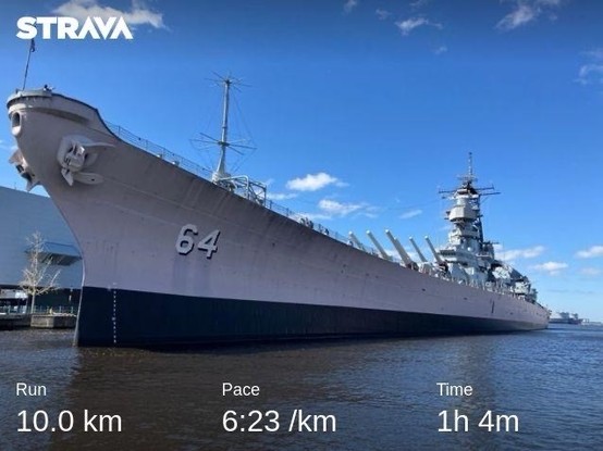 A battleship, the USS Wisconsin, docked at a pier under clear blue skies with small dotted clouds speckled about. My running stats are along the bottom: 10km in 1:04 for an average pace of 6:23/km