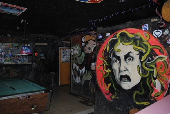 Old photo of the dive bar Lola's in Houston. There's a beat-up pool table on the left & a giant Medusa head & Beans Barton murals on the wall on the right. The walls are black & covered in graffiti & everything is dirty & grungy & AWESOME.