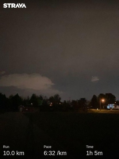 Overcast skies reflect light pollution to make it seem like dusk. In the distance, across the open field are street lights and tiny houses. My run stats are along the bottom: 10km in 1:05 for an average pace of 6:32/km