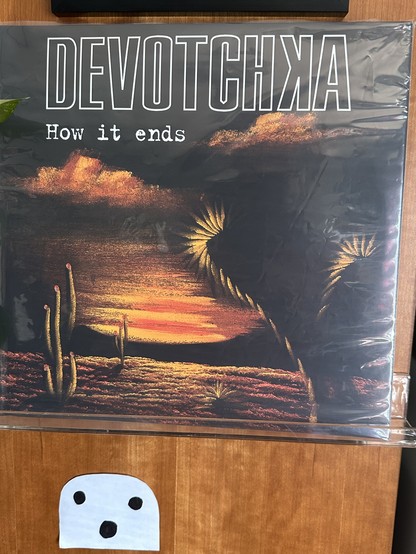 Cover to How it ends by the band Devotchka. Features a painting of a desert sunset with clouds and cacti.